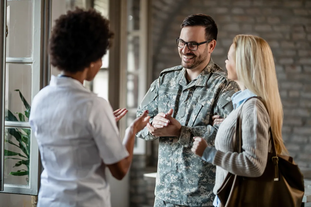 Service member in military uniform speaking with two civilians at a doorway