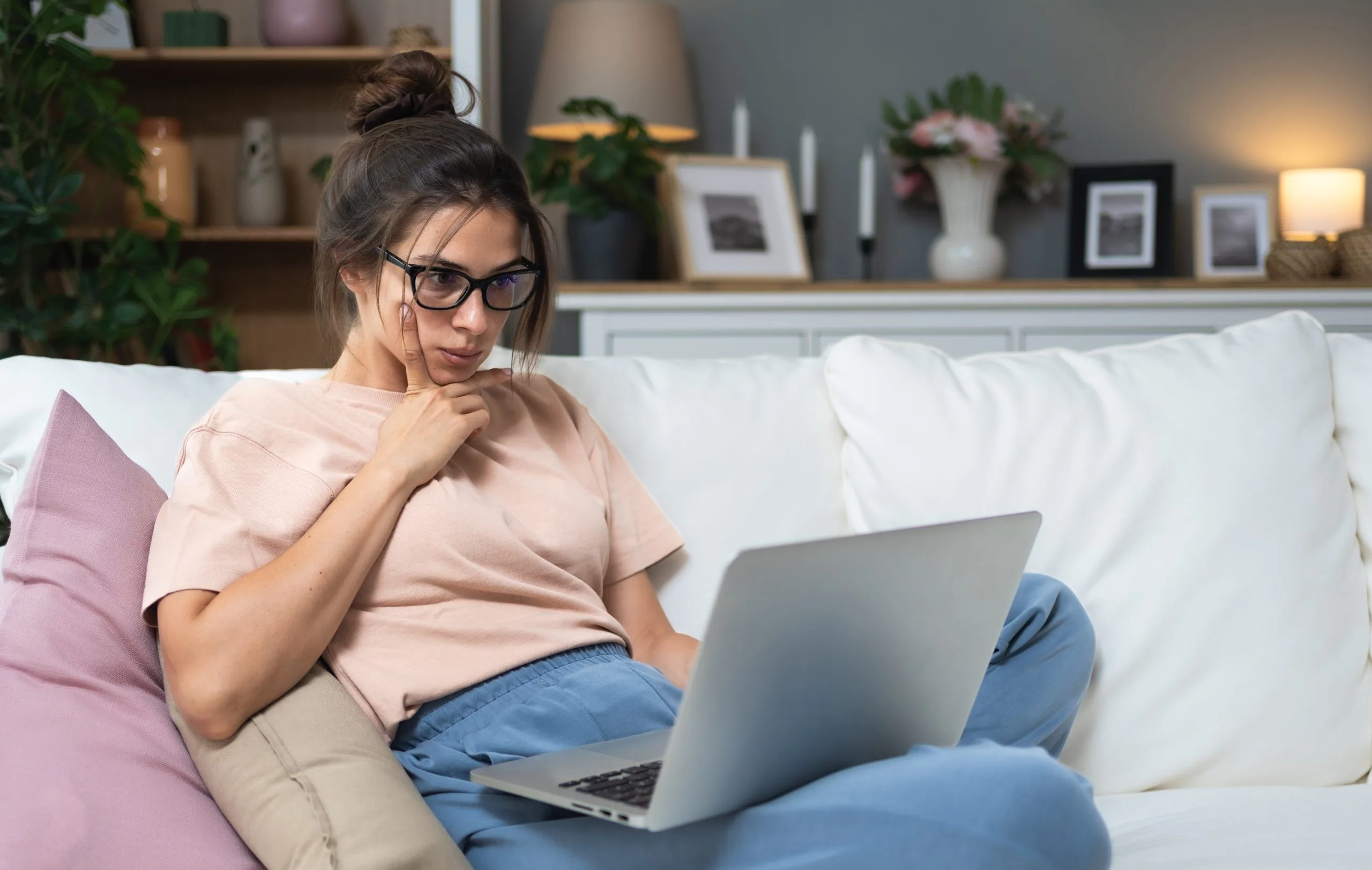 Woman with glasses working on laptop while sitting on a couch at home