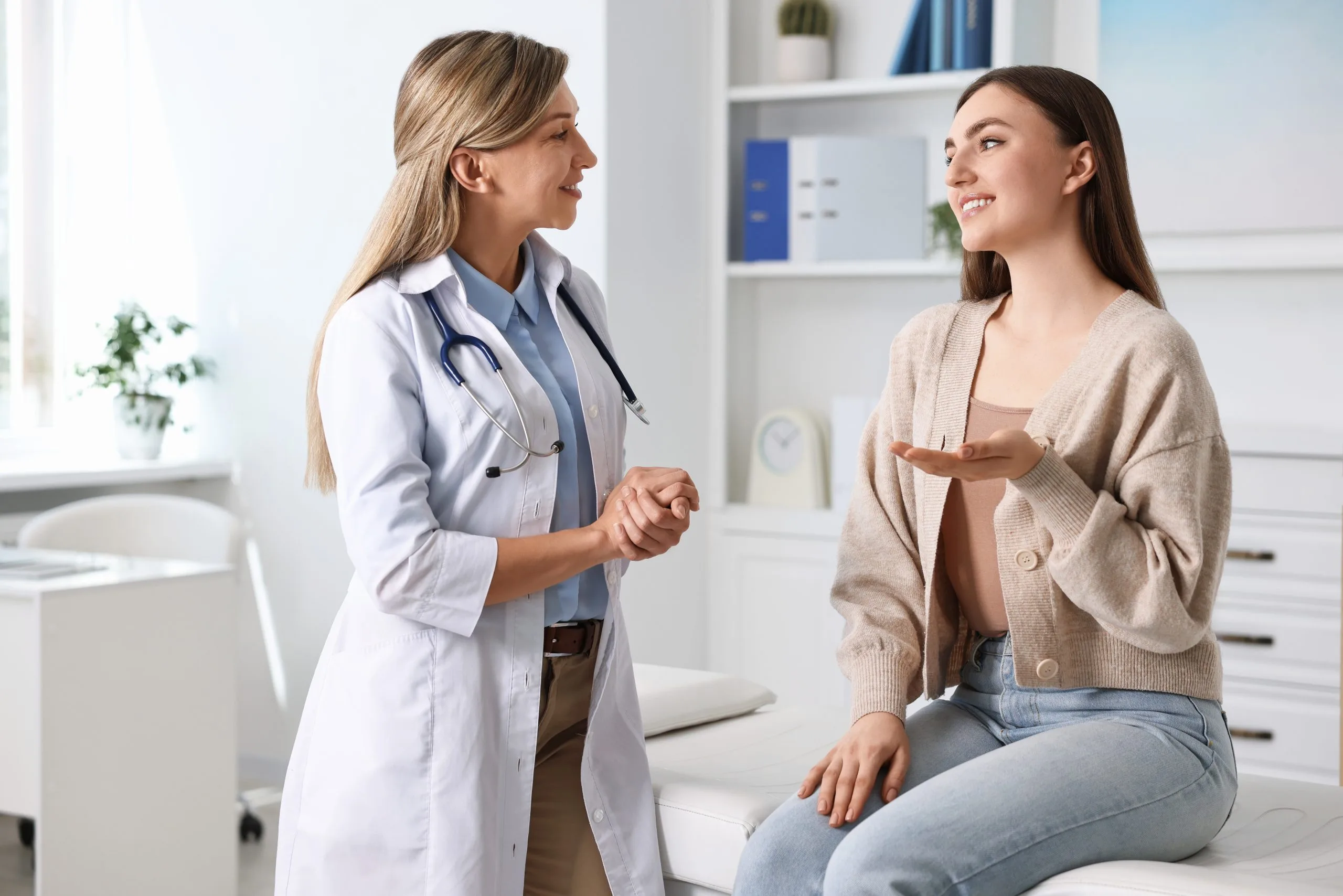 Female doctor with stethoscope shakes hands with smiling female patient in medical office