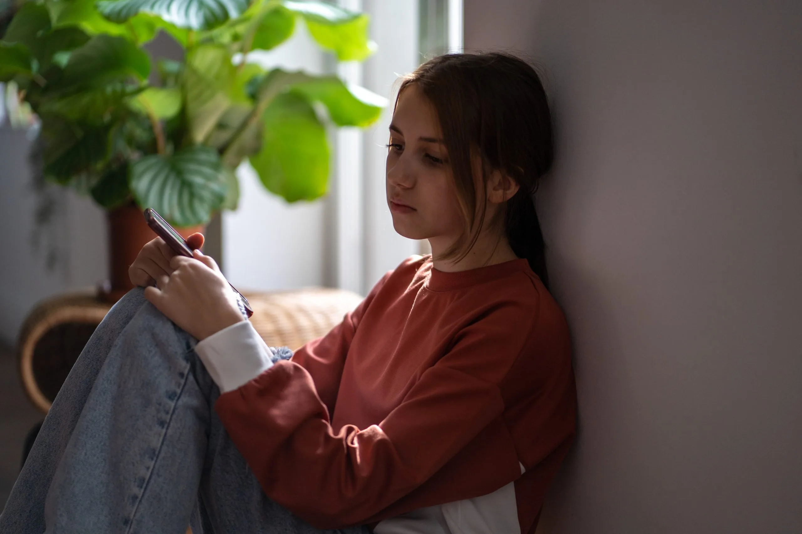 Teen girl sitting by a window holding a pen, appearing thoughtful or sad
