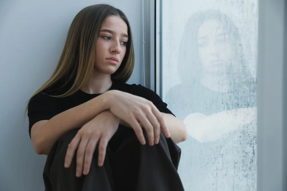 Teen girl sitting by a window with a contemplative expression