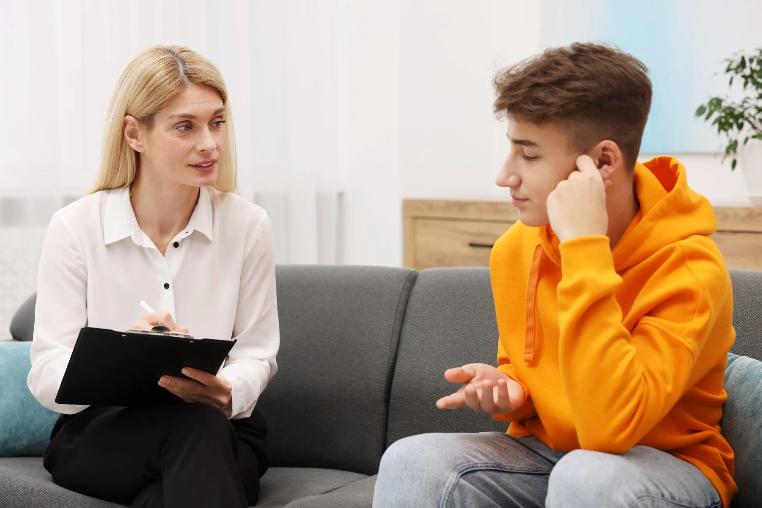 Psychologist talking with a teenage boy on a sofa in an office during a TMS consultation