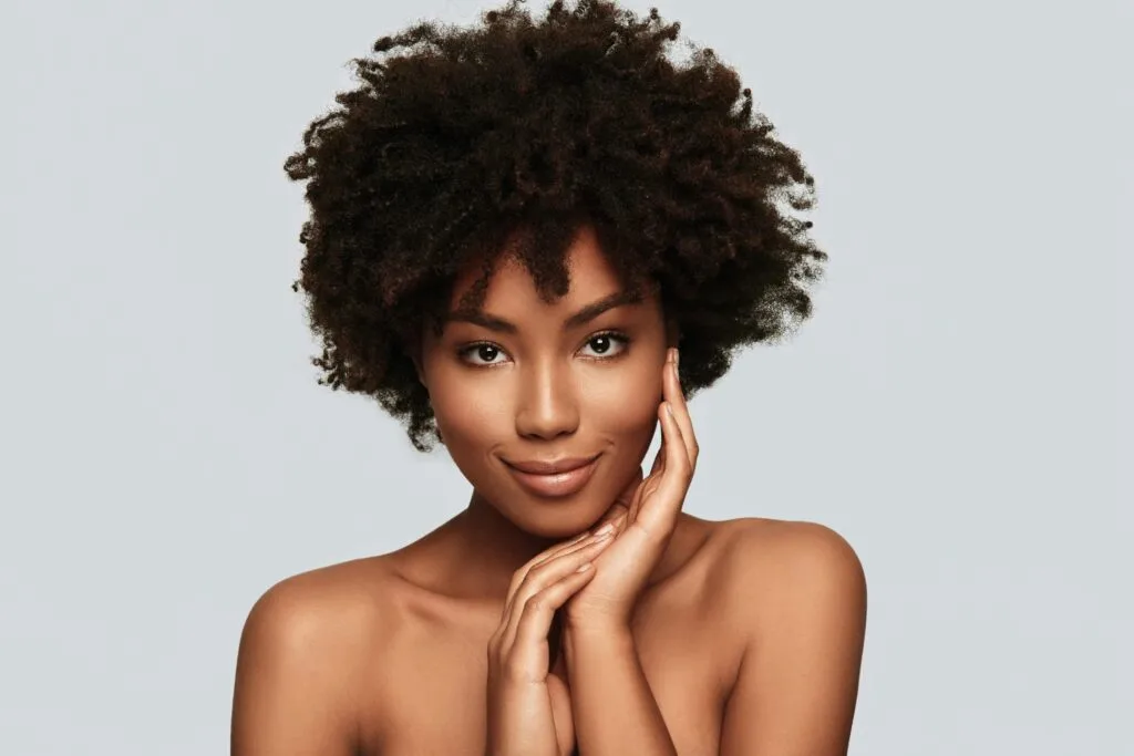 Woman with clear skin touching her face against neutral background