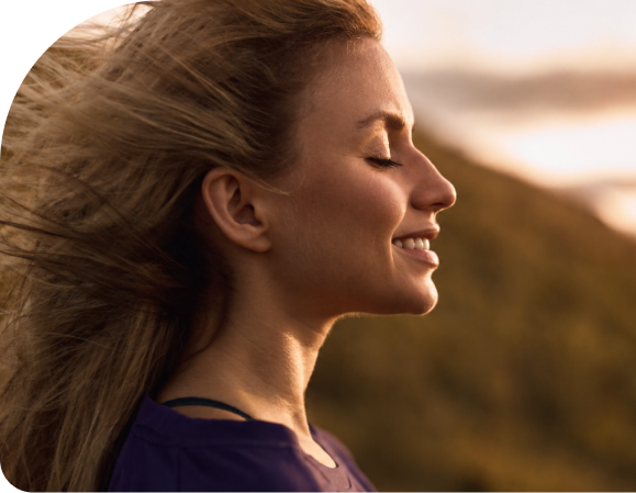 Woman in profile smiling with eyes closed in outdoor setting