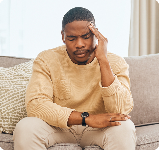 Man sitting on couch holding his head, appearing stressed or anxious