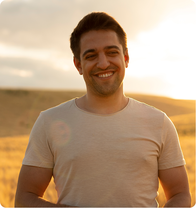 Smiling man in beige t-shirt outdoors at sunset