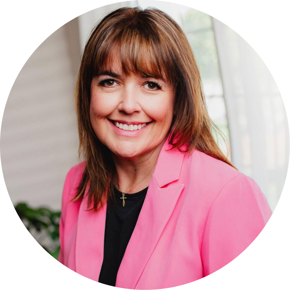 Woman with brown hair and bangs smiling, wearing pink blazer over black shirt