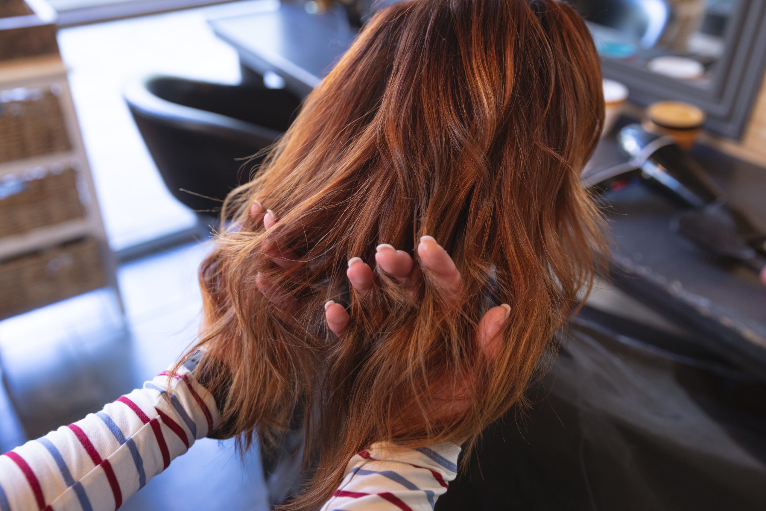 Stylist's hand touching client's voluminous reddish-brown wavy hair in salon