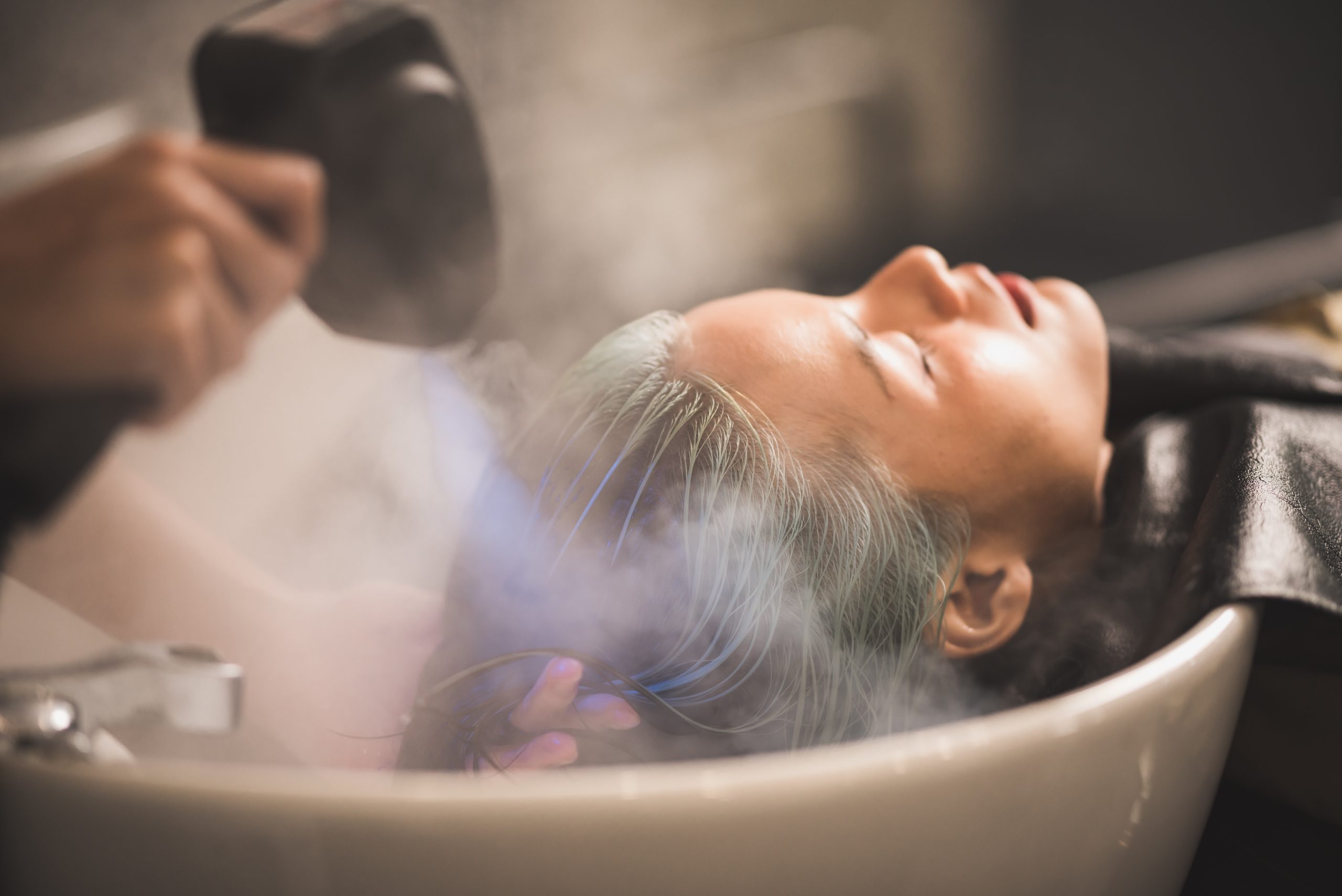 Stylist blow-drying client's gray hair during salon service