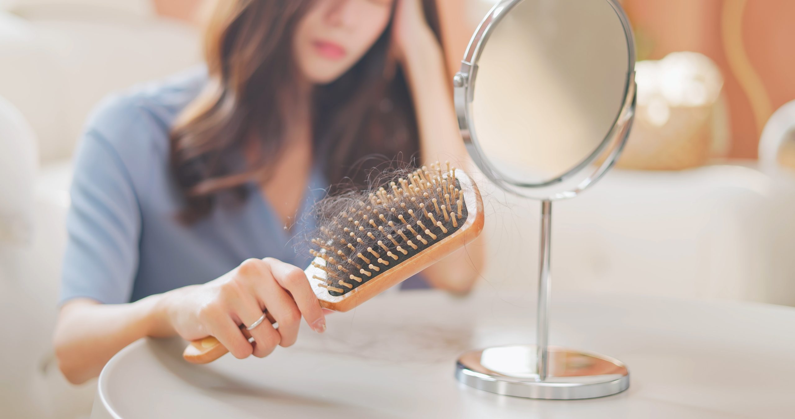 Woman holding paddle brush with collected hair strands while looking in mirror