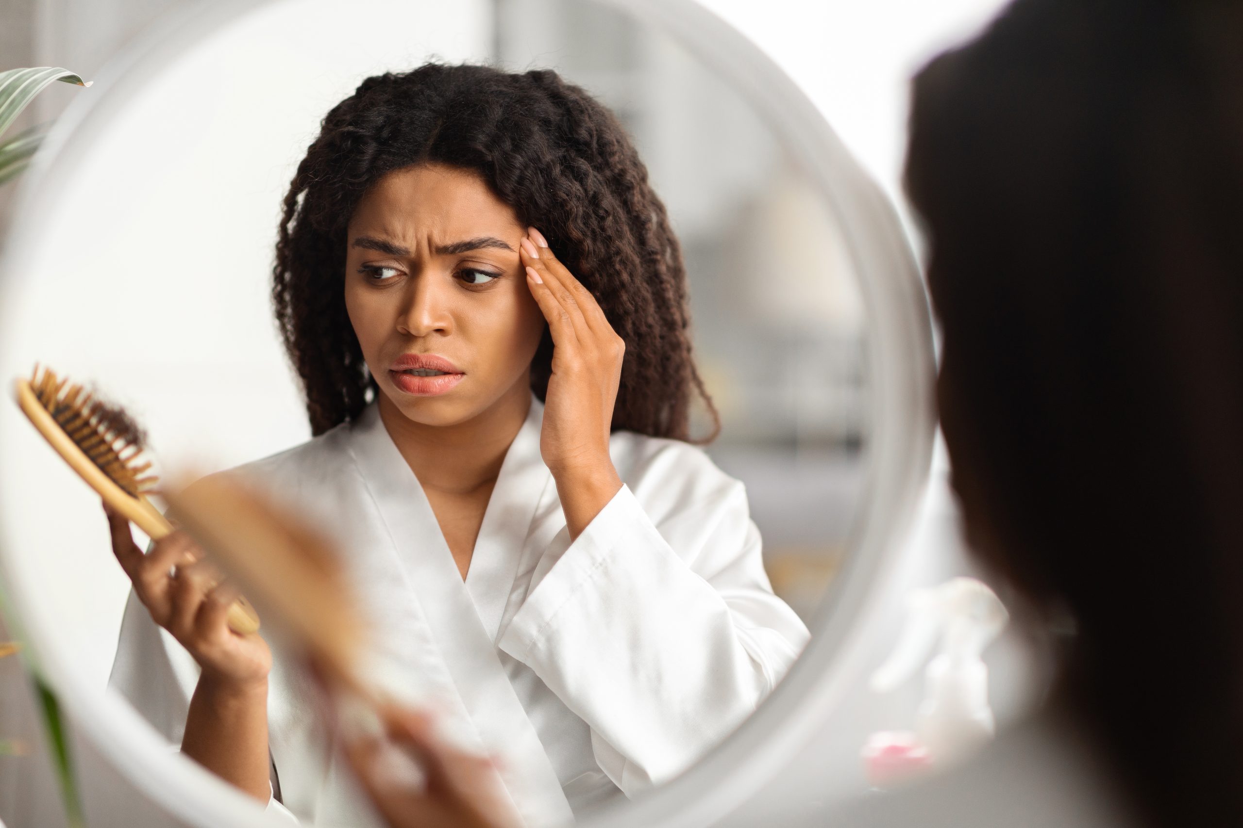 Woman looking in mirror examining her hair with concerned expression