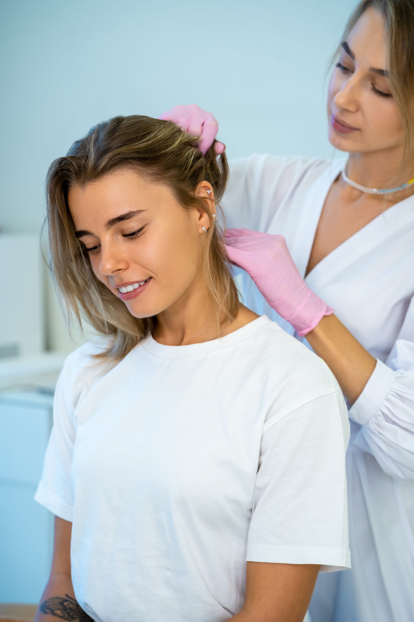 Healthcare provider in pink gloves examining patient's scalp during consultation