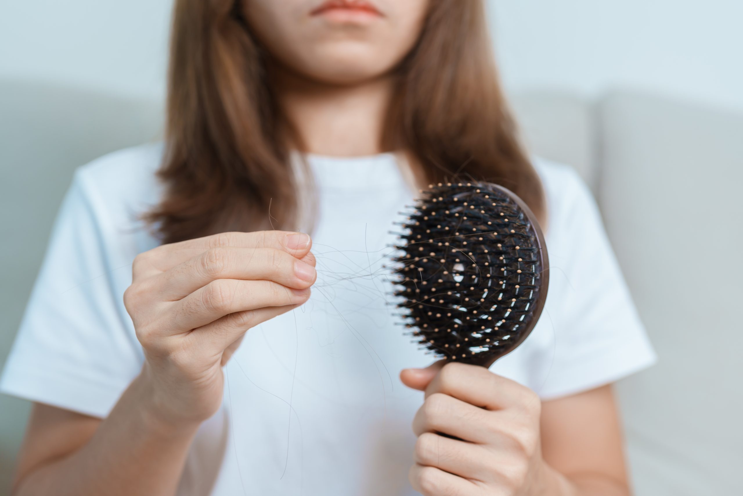 Woman holding round paddle brush showing strands of hair caught in bristles