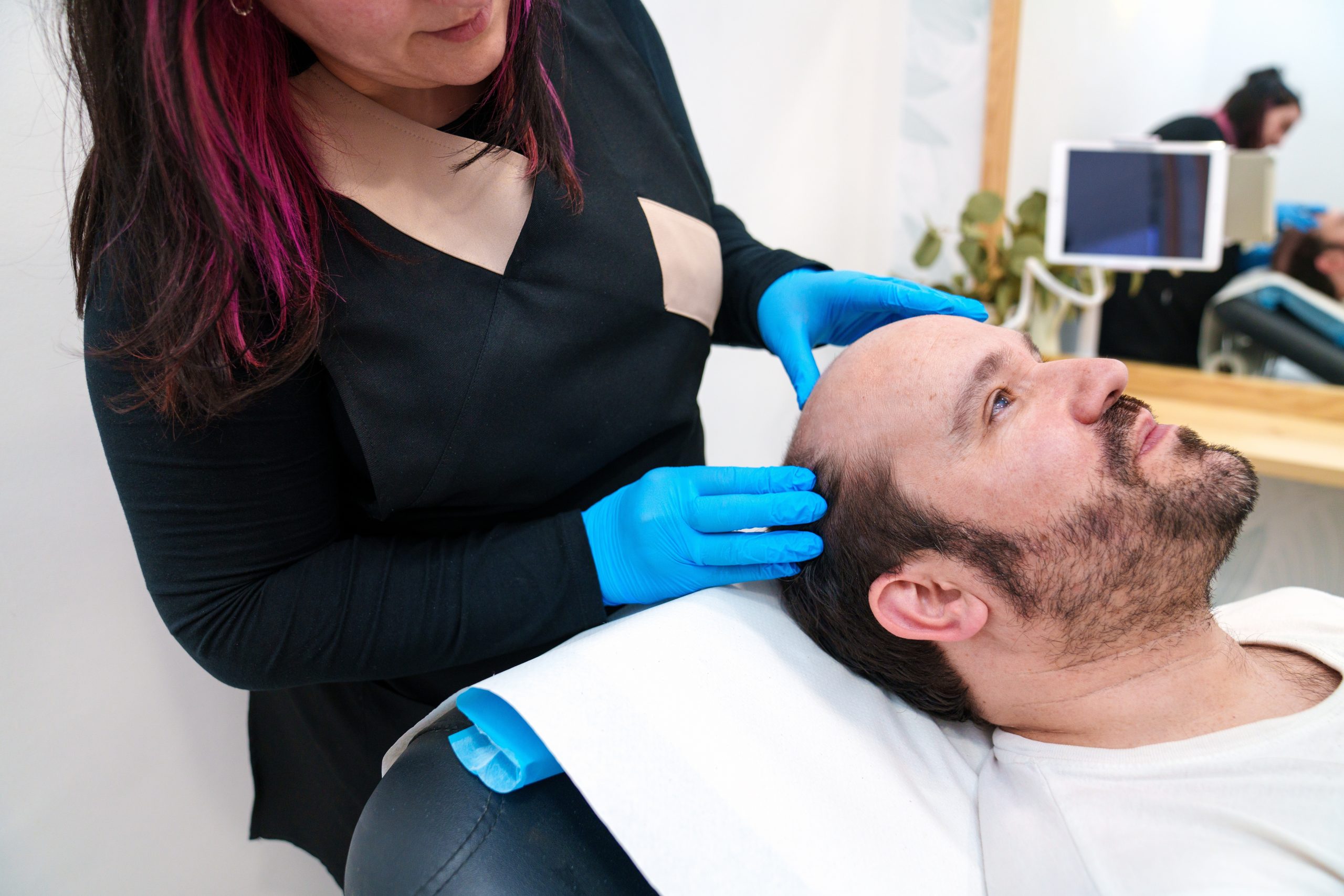 Clinician in blue gloves examining a male patient's scalp before a hair restoration procedure