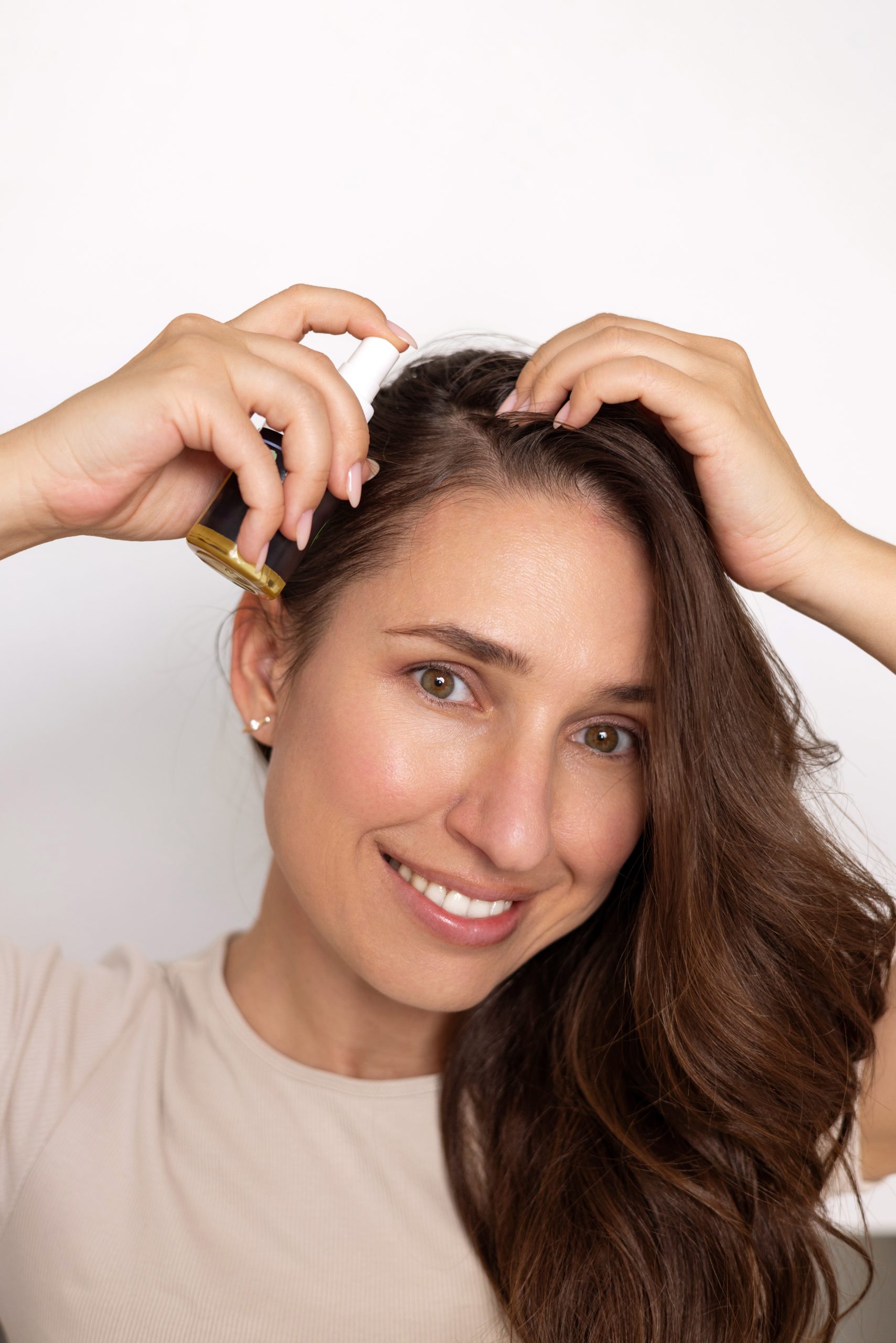 Woman applying hair serum or oil to her scalp with dropper applicator