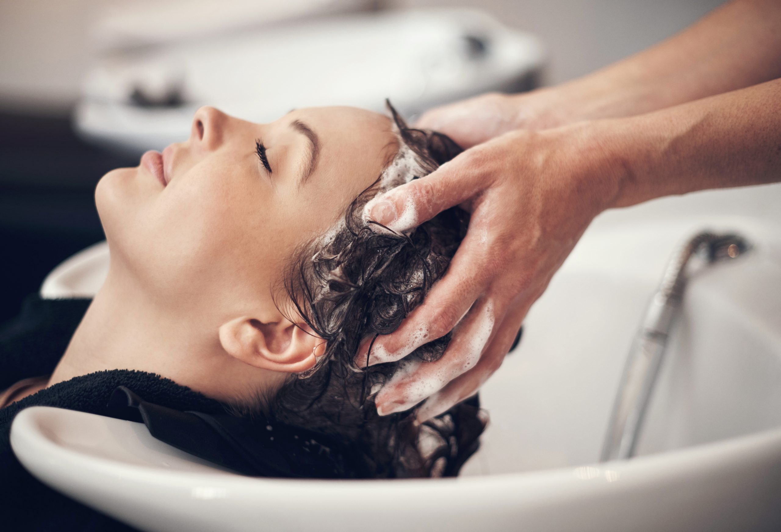 Stylist massaging client's scalp with lathered shampoo at salon sink