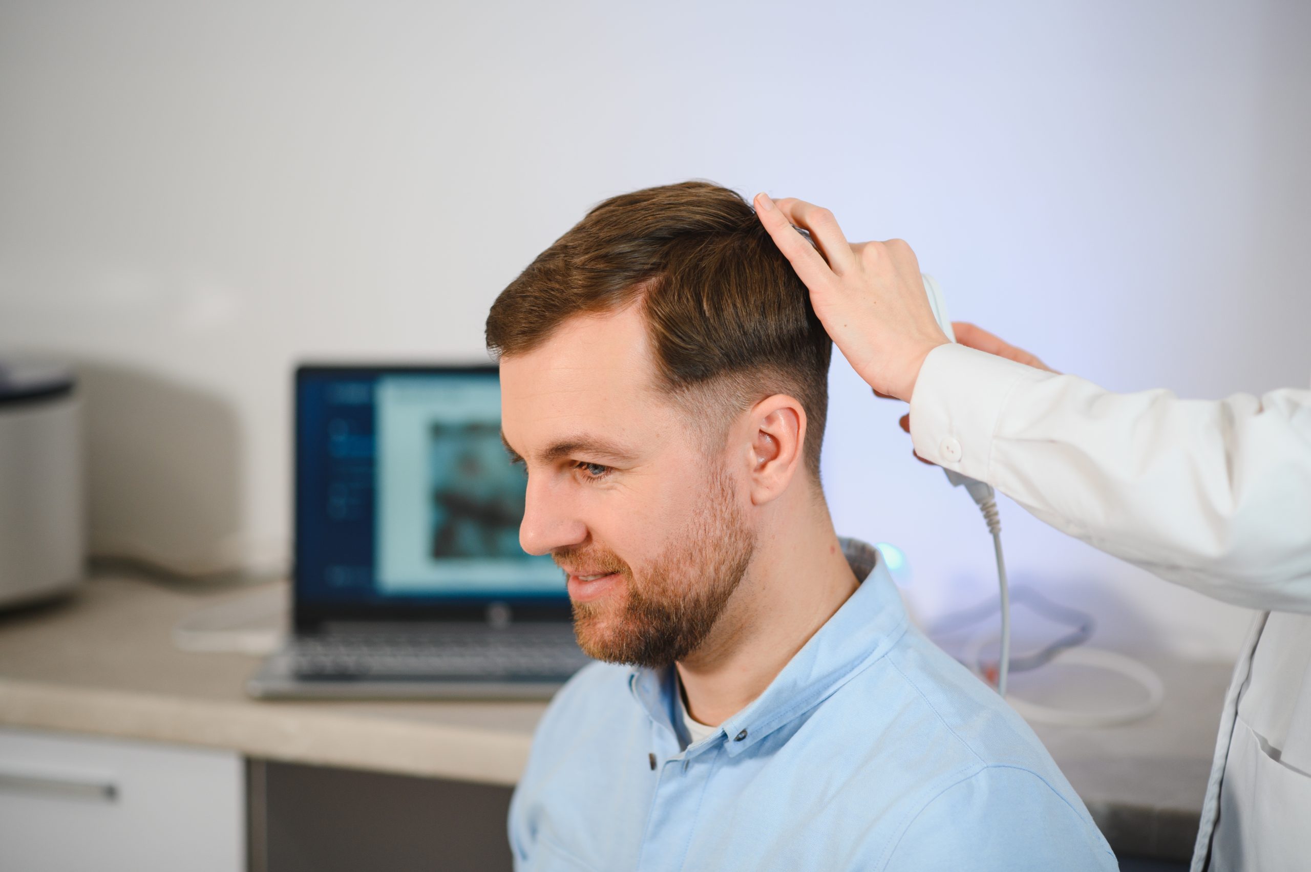 Clinician examining patient's scalp and hair in medical office with computer in background
