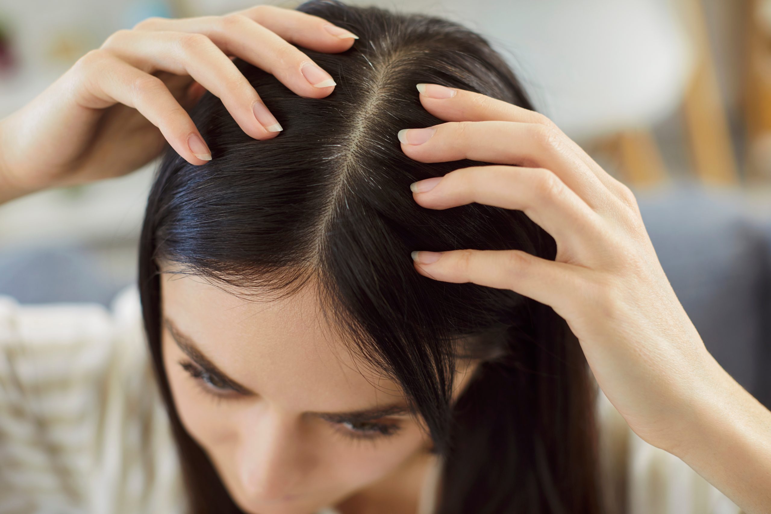 Woman examining her scalp with both hands, checking for hair or scalp concerns