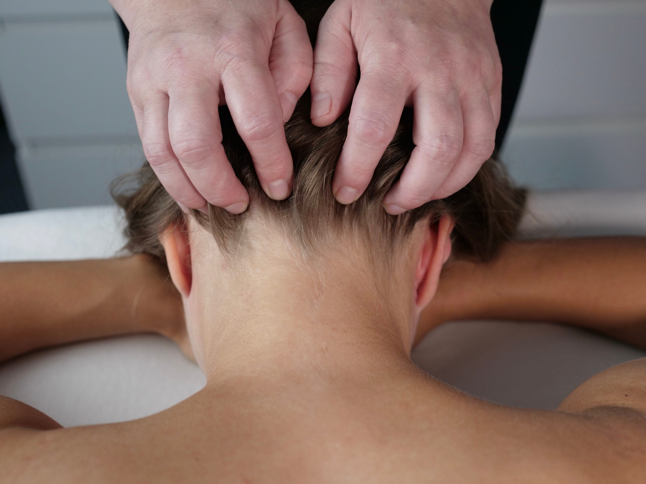 Therapist performing scalp massage on male patient lying face down on treatment table