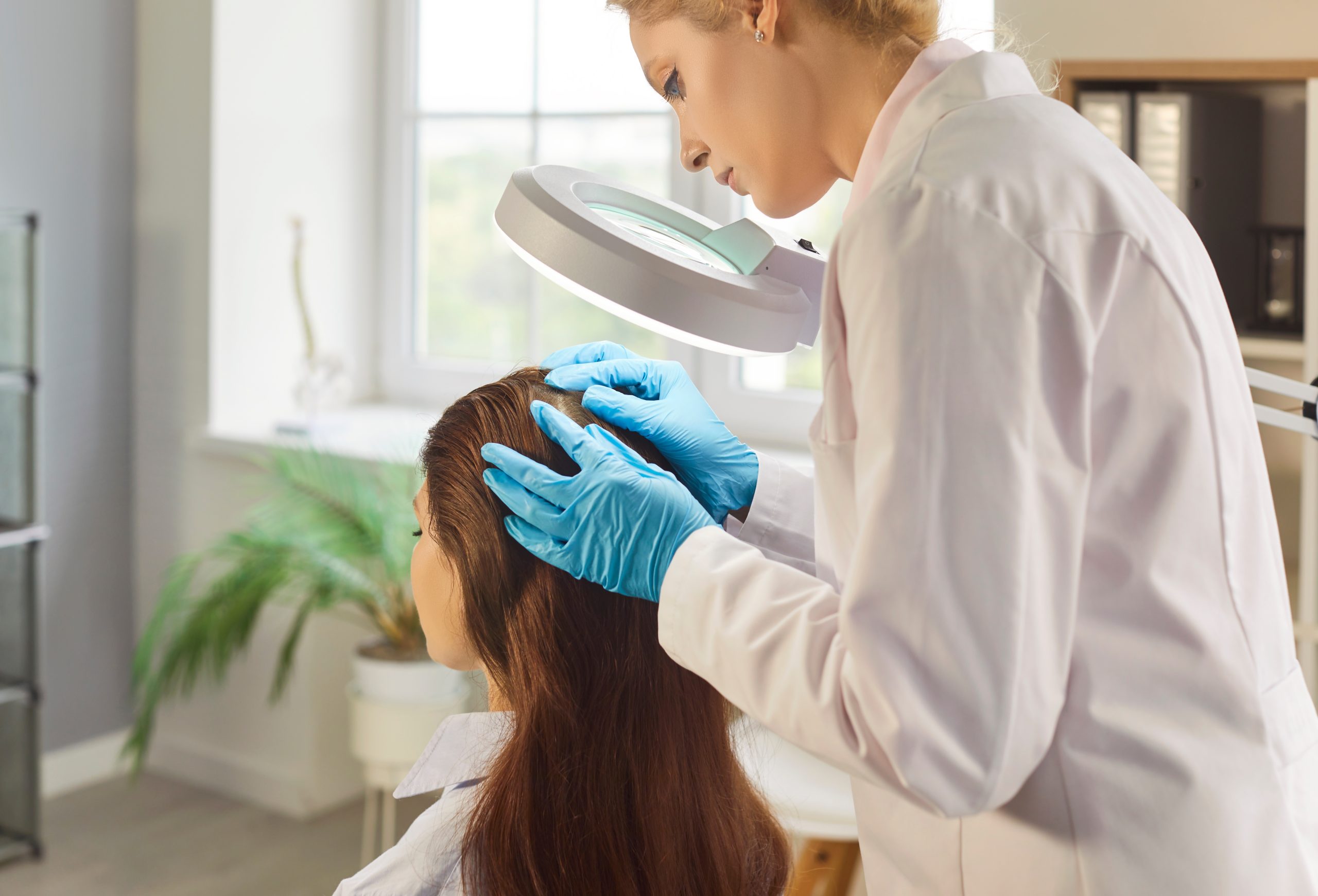 Dermatologist examining patient's scalp with magnifying lamp in clinic