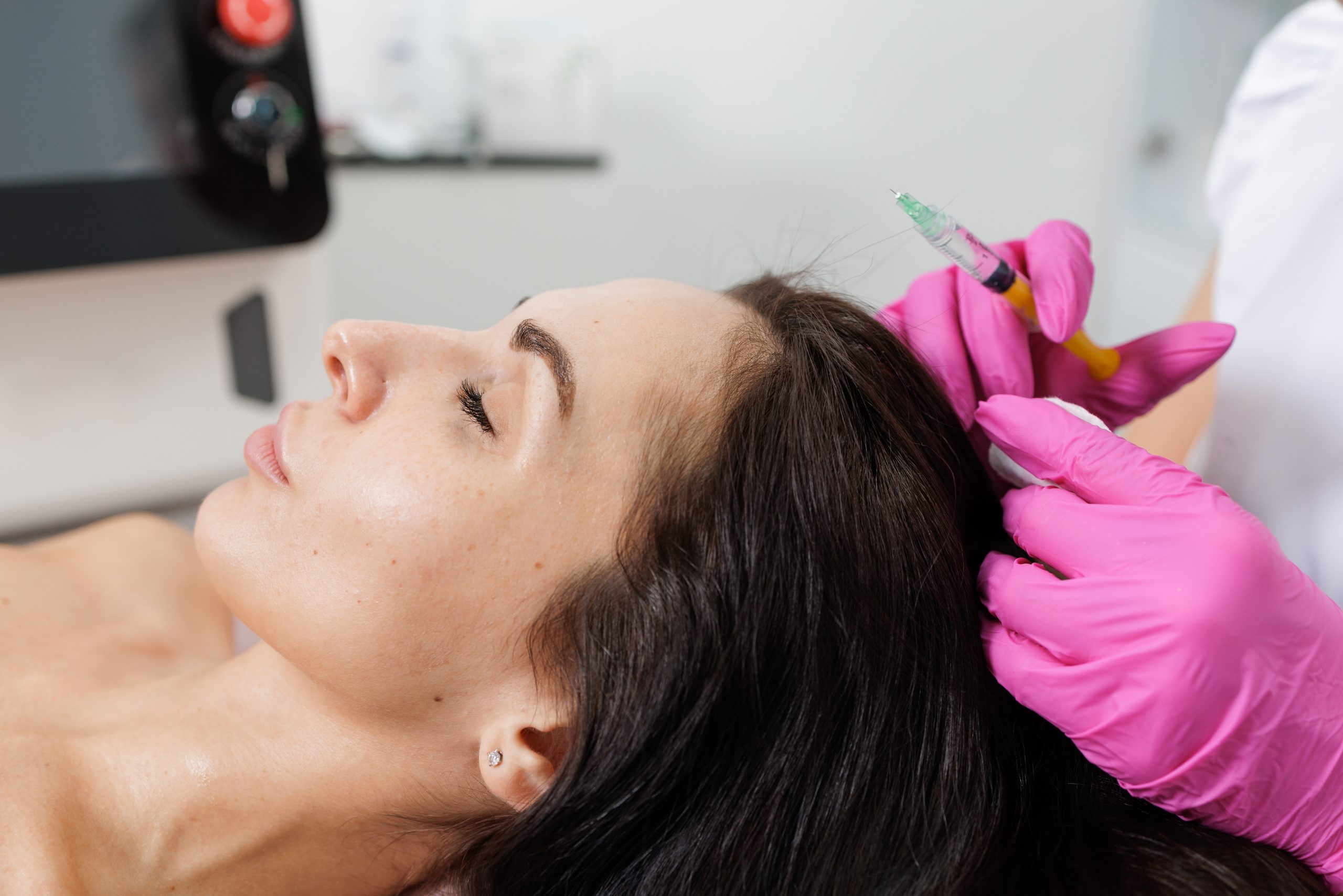 Practitioner in pink gloves administering scalp injection to reclined patient