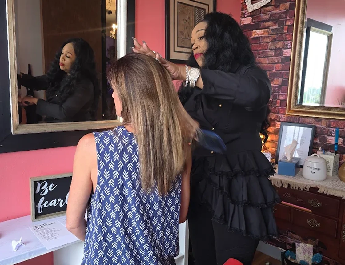 Practitioner styling a client's long hair at a salon mirror with pink accents
