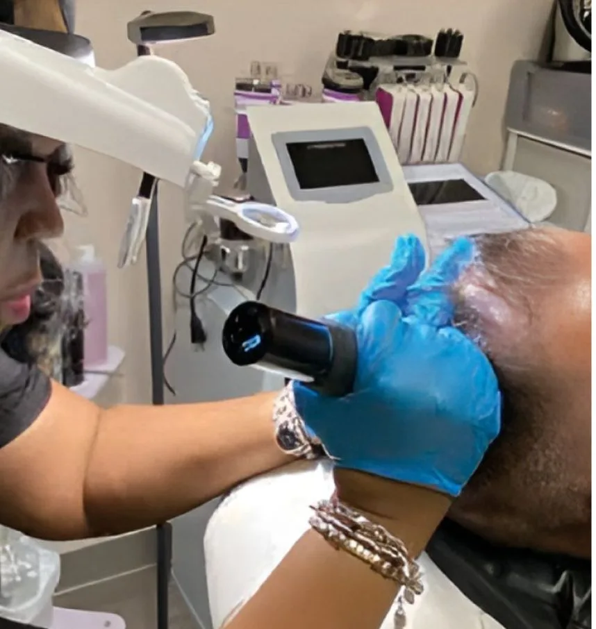 Practitioner in blue gloves using handheld device on patient's scalp in clinical setting