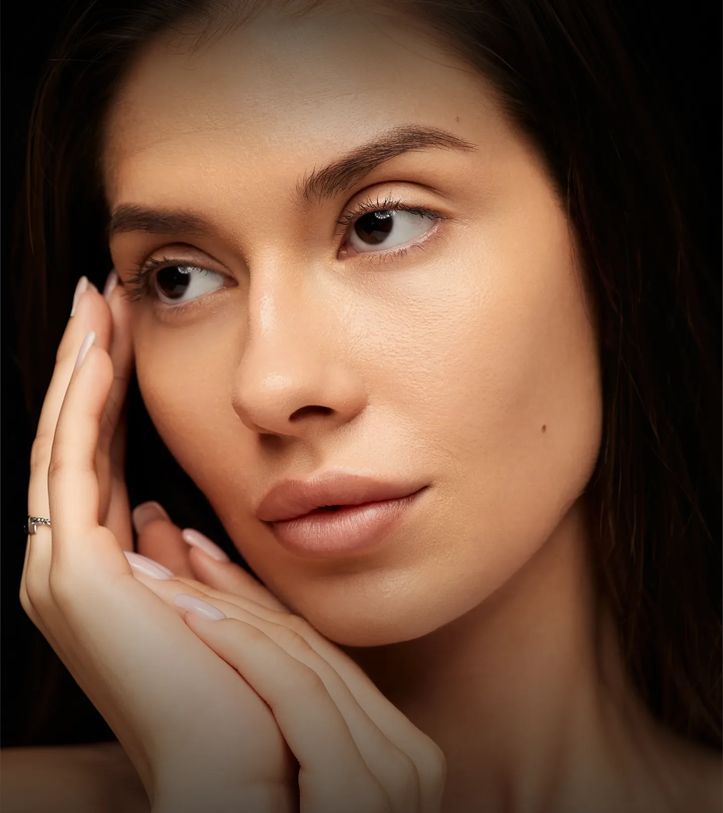 Woman with dark hair touching her face, displaying clear skin and well-groomed eyebrows