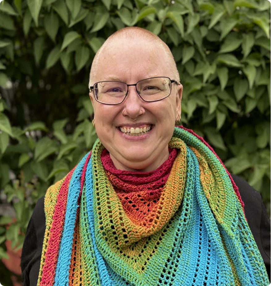 Therapist wearing glasses and colorful rainbow scarf smiling in front of green plants