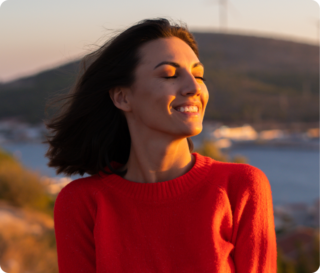 Woman smiling outdoors at sunset in red sweater