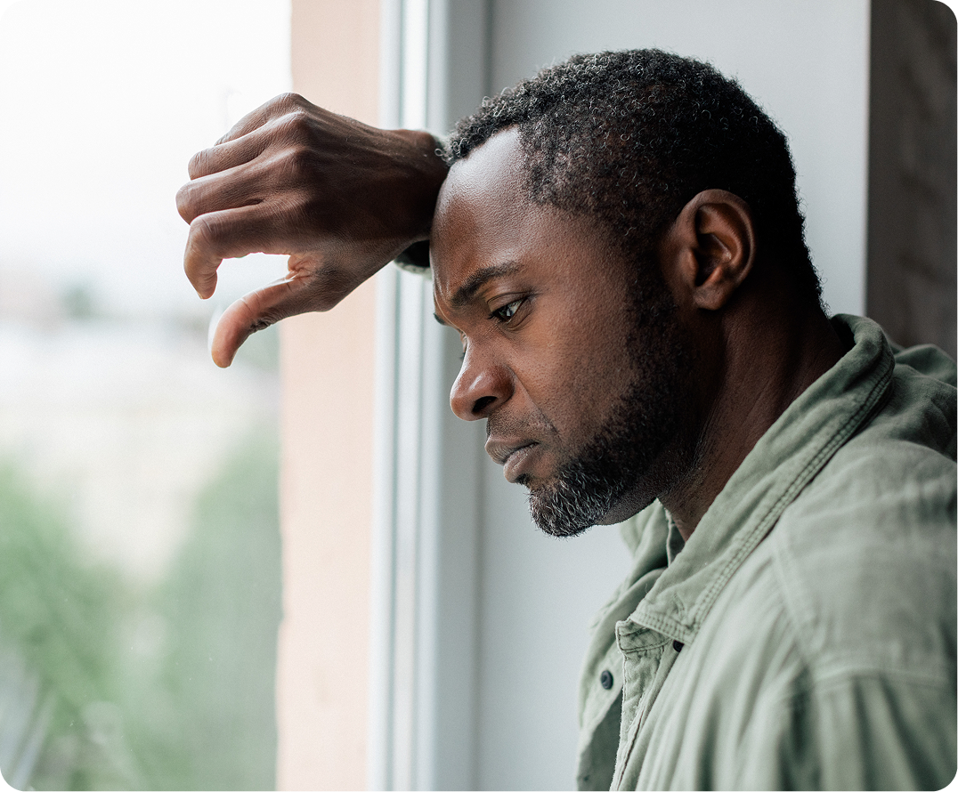 Man with hand to forehead looking distressed while gazing out a window