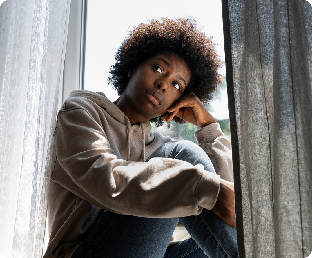Woman sitting by window with thoughtful expression, hand to face, looking upward