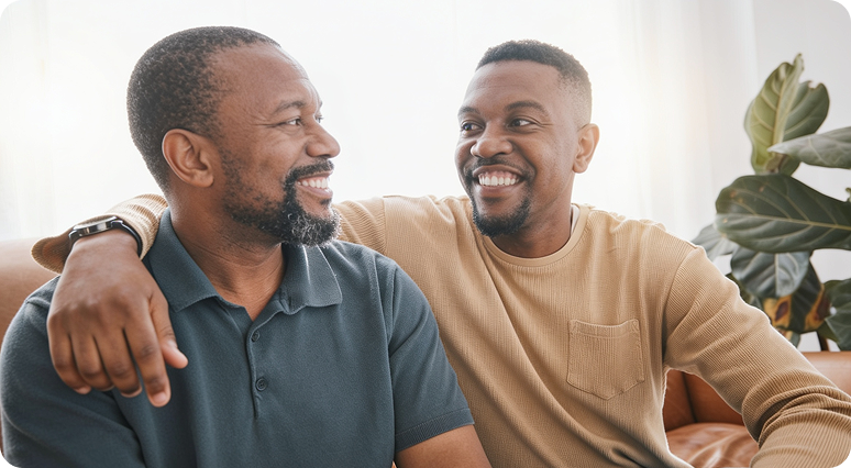 Two men smiling together indoors with potted plant in background