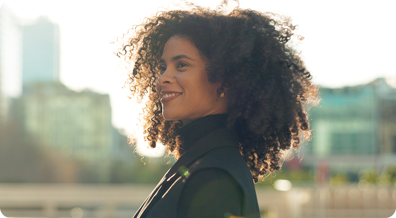 Woman with curly hair smiling in profile against urban skyline