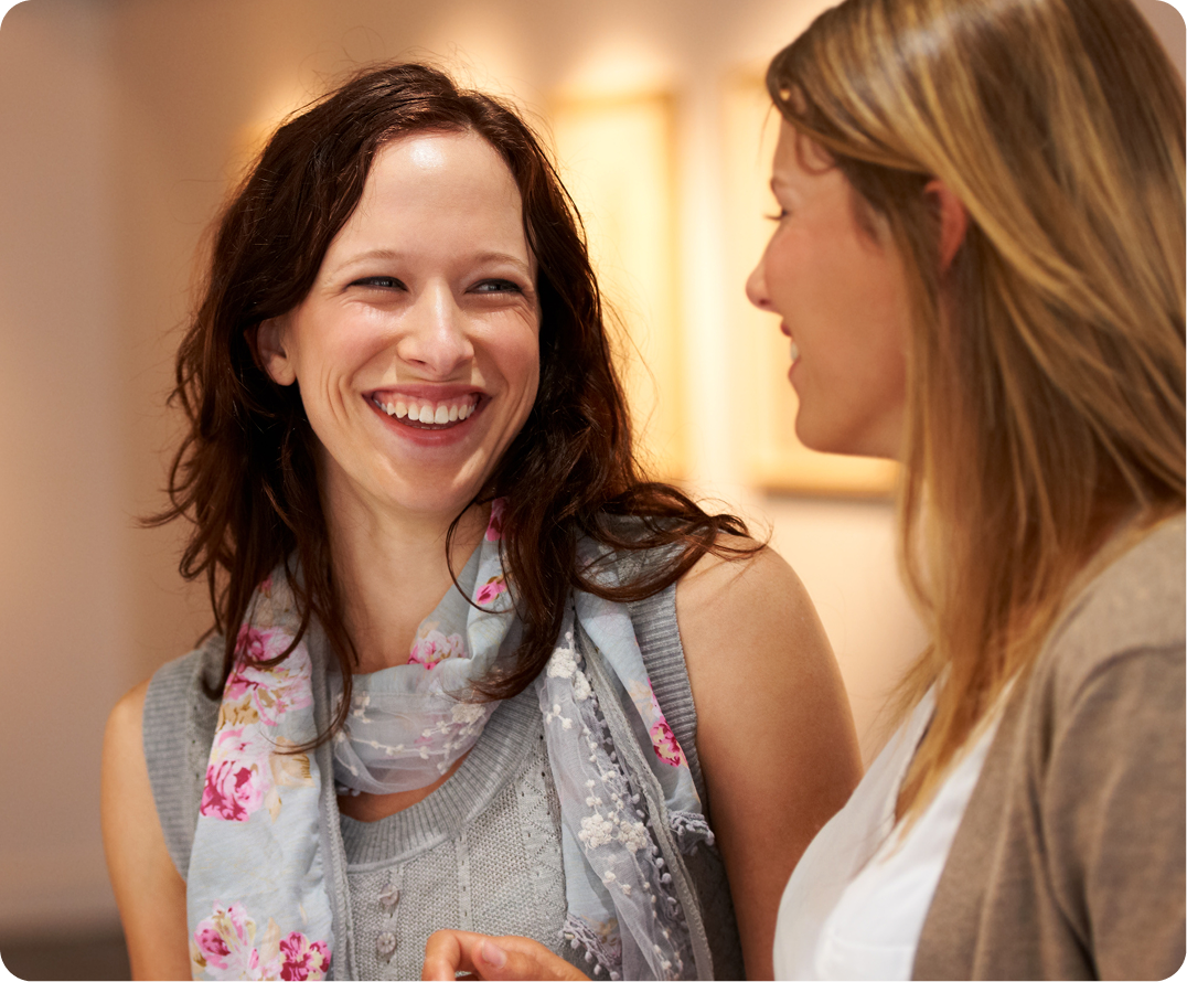 Two women smiling at each other in conversation in a warm indoor setting