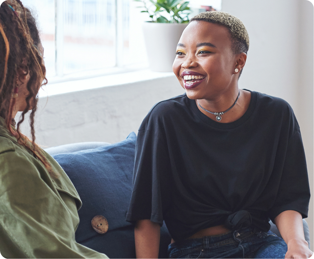 Two women smiling while conversing on blue couch in sunlit office setting