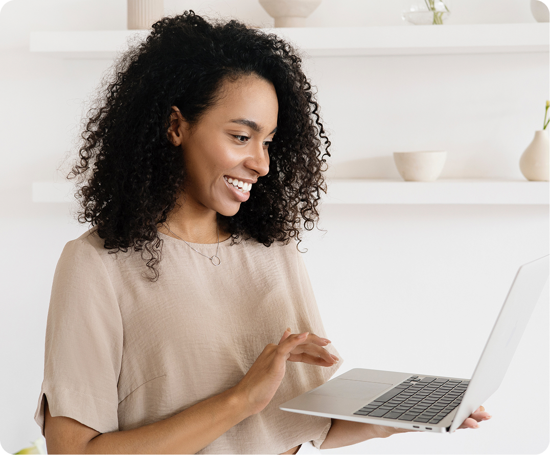 Woman with curly hair smiling while using laptop at home