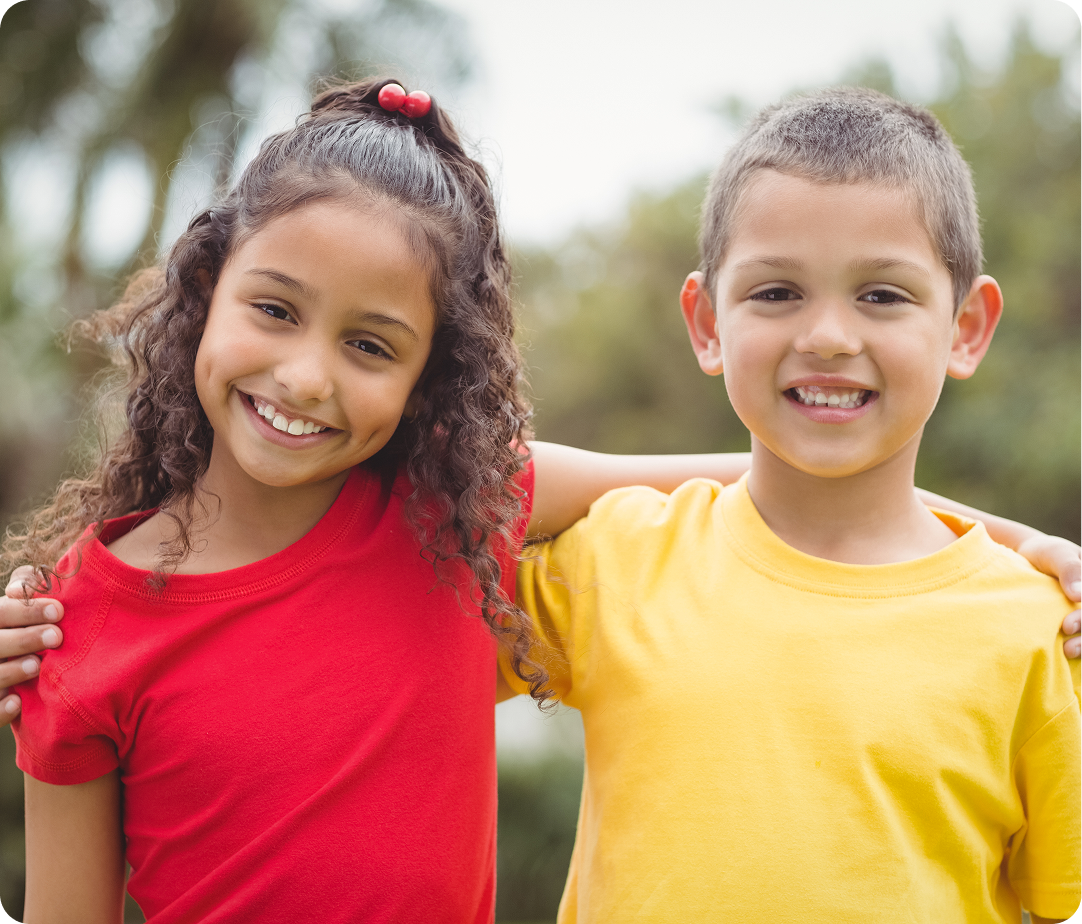 Two smiling children standing together outdoors with arms around each other