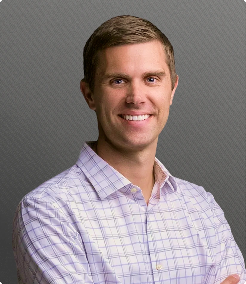 Dr. Joshua Hustedt, smiling man wearing light purple checkered shirt against gray background