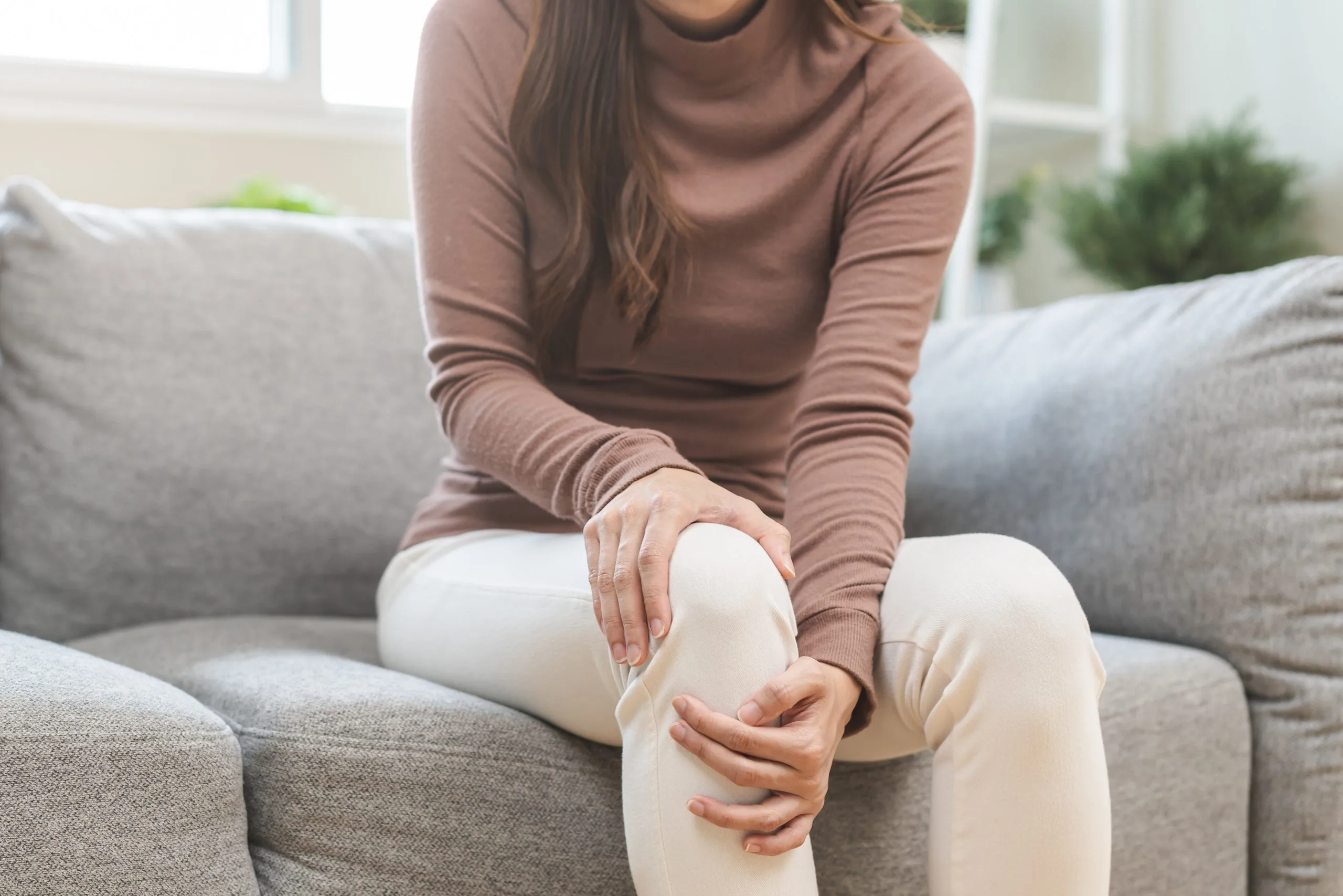 Woman sitting on a couch holding her knee with both hands