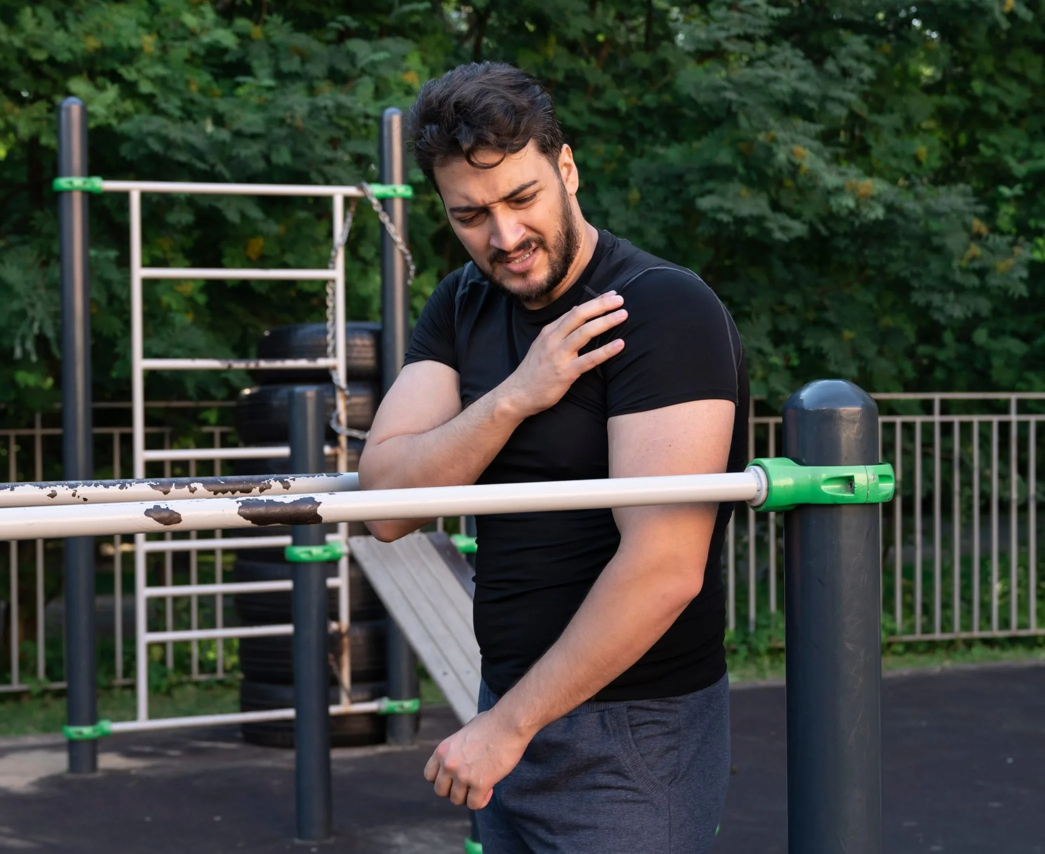 Man at outdoor exercise equipment holding his shoulder in discomfort