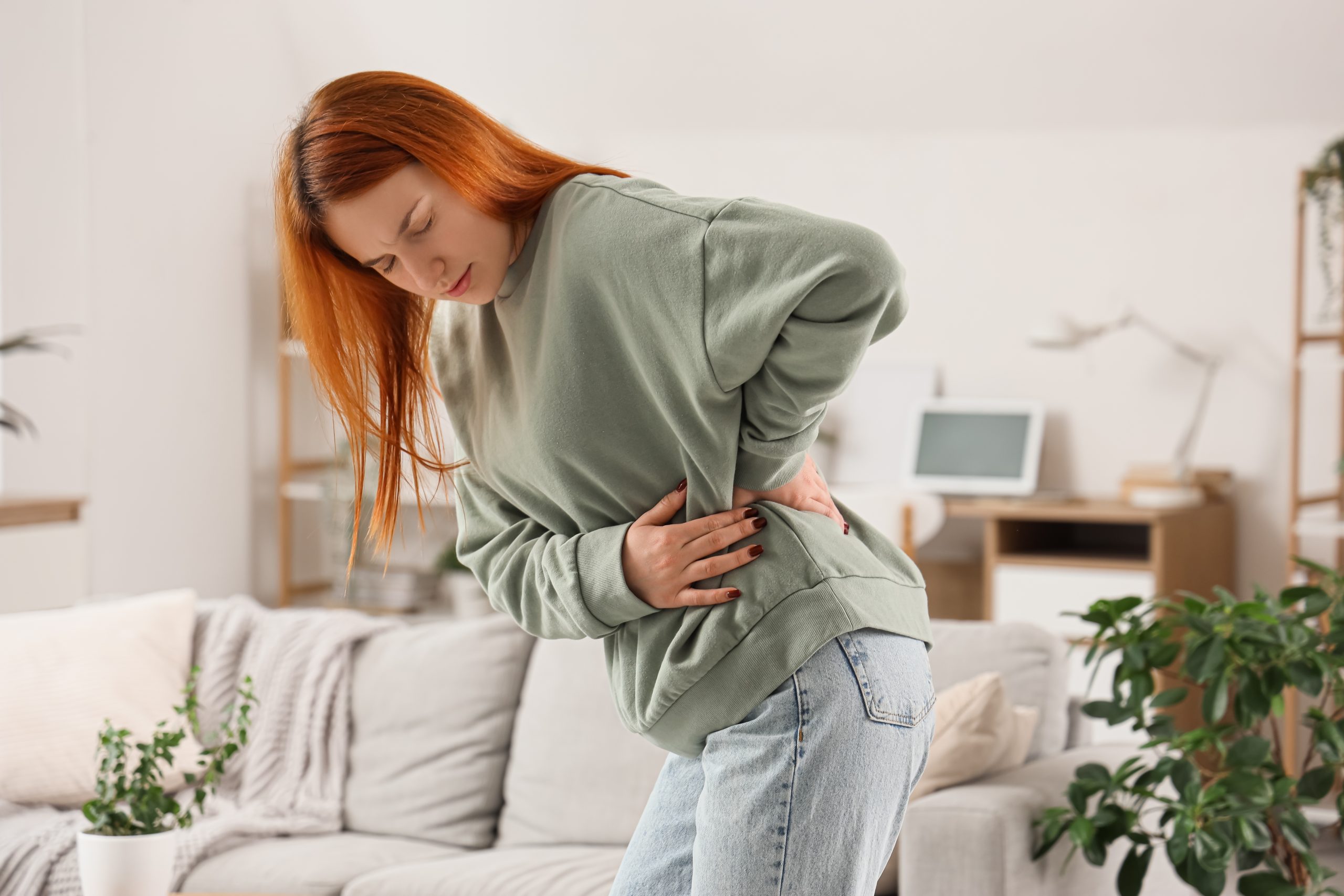 Woman standing indoors holding her lower abdomen with both hands