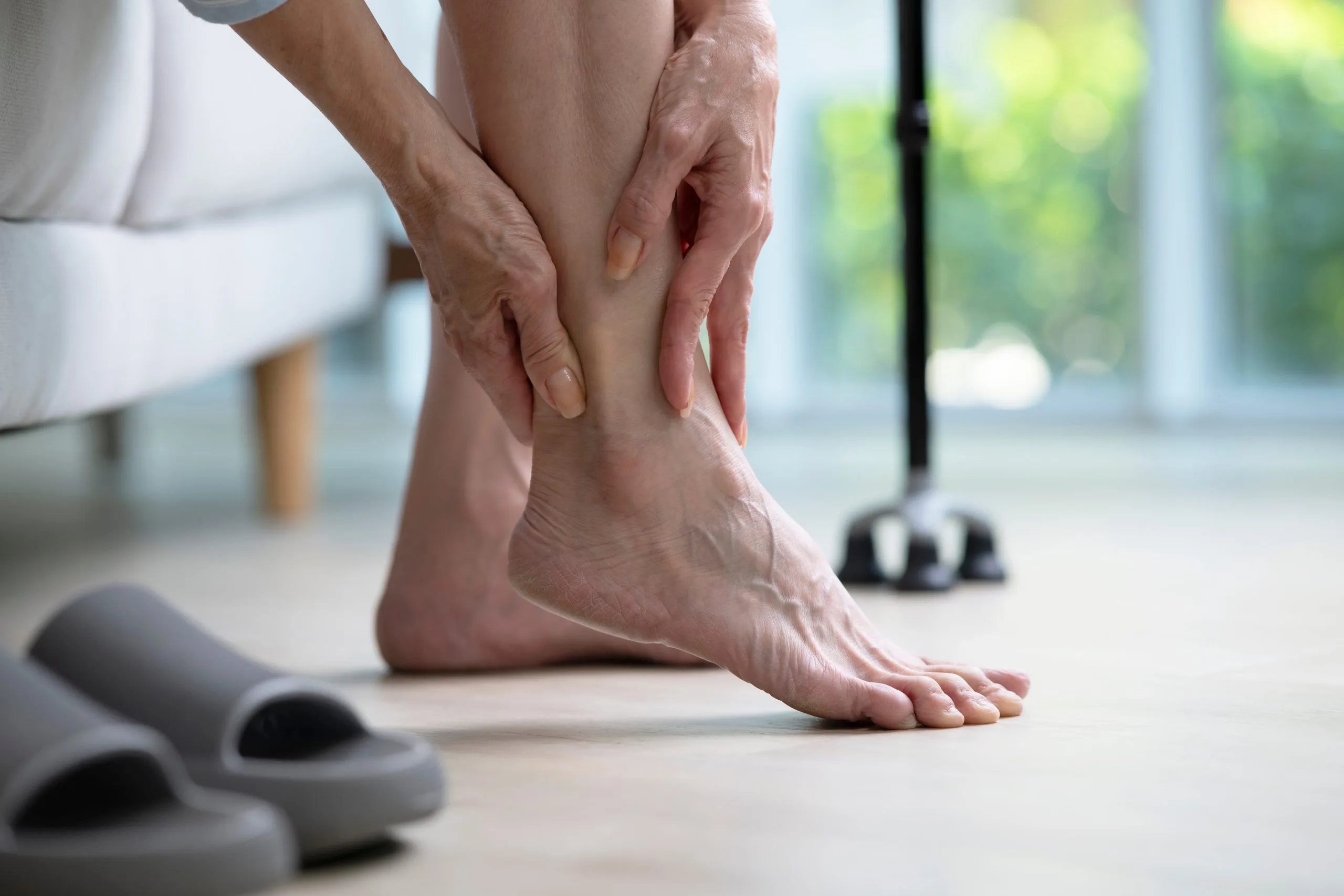 Clinician palpating a patient's ankle during examination in a bright clinical setting
