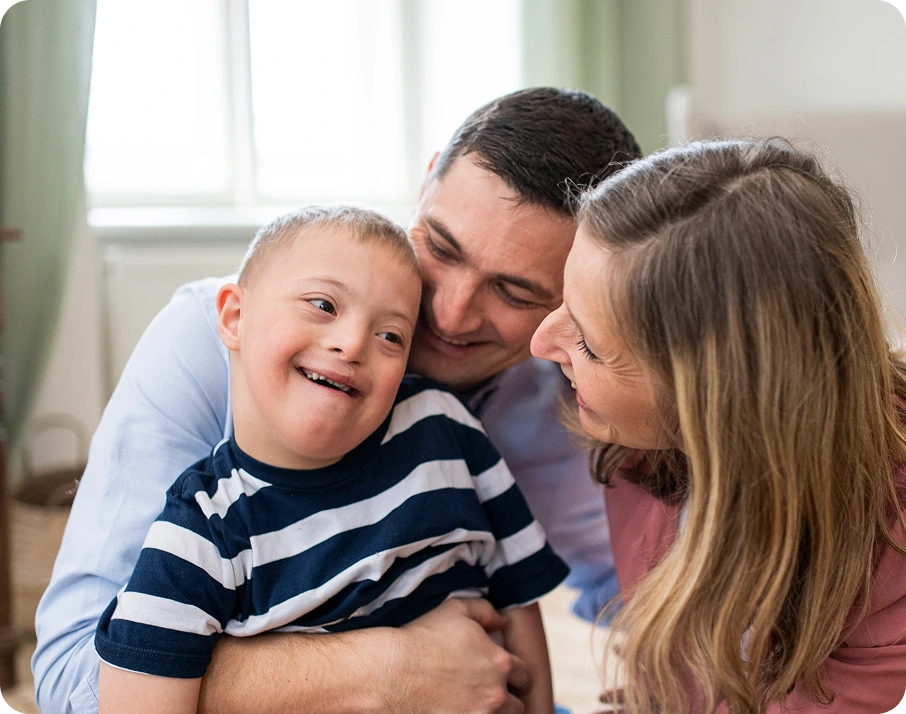 Parents smiling while holding their young son with Down syndrome in a bright home setting