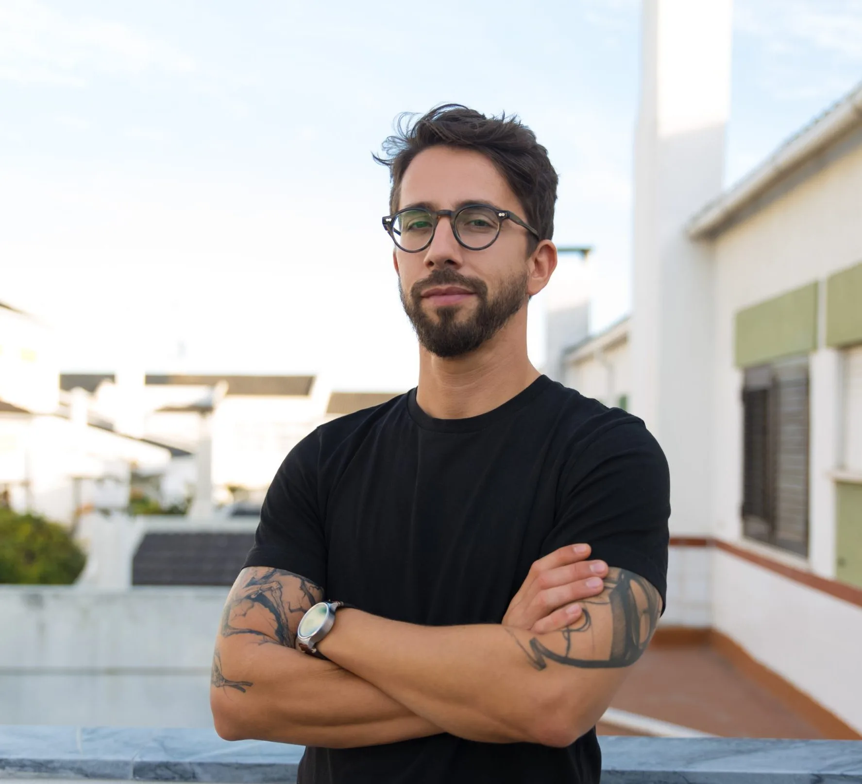 Man with glasses and crossed arms on a rooftop