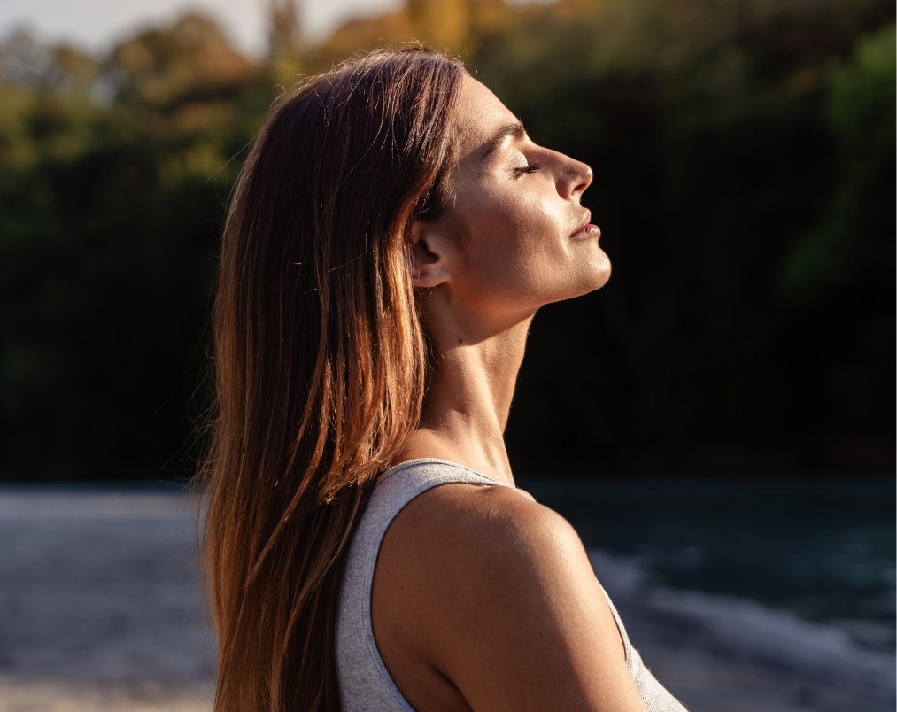 Woman with long hair in profile facing sunlight outdoors near water