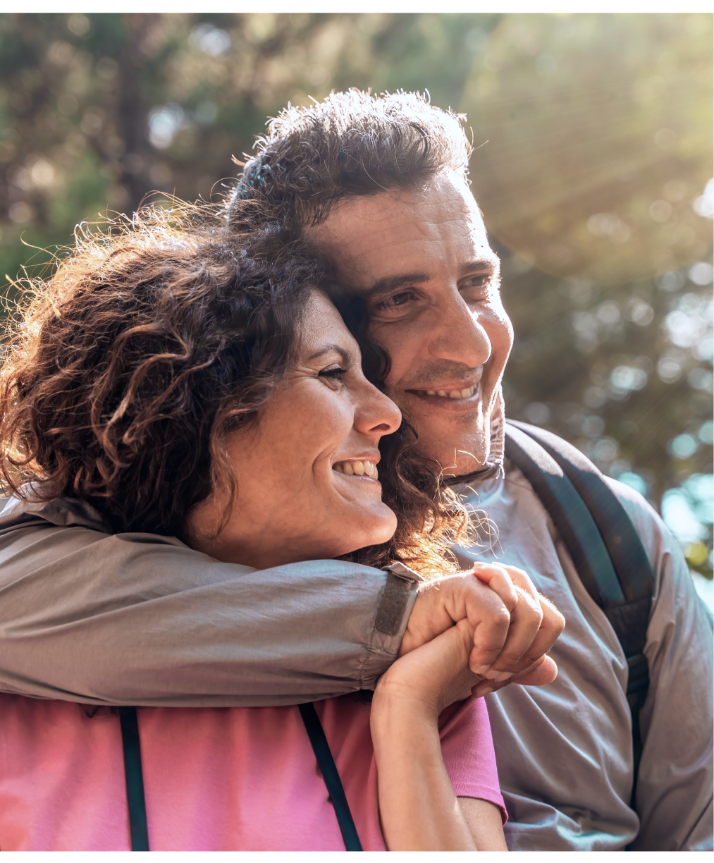 Smiling couple embracing outdoors with trees in soft-focus background