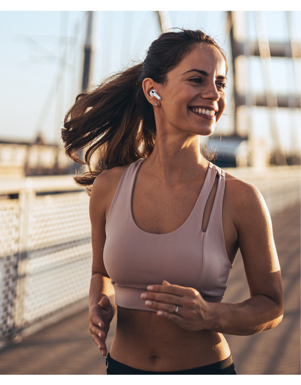 Woman wearing wireless earbuds jogging on sunny boardwalk