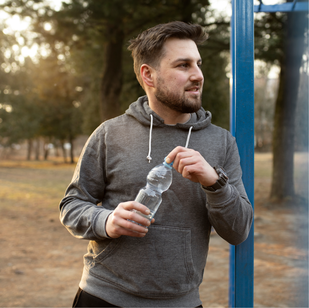 Man holding water bottle outdoors in park setting