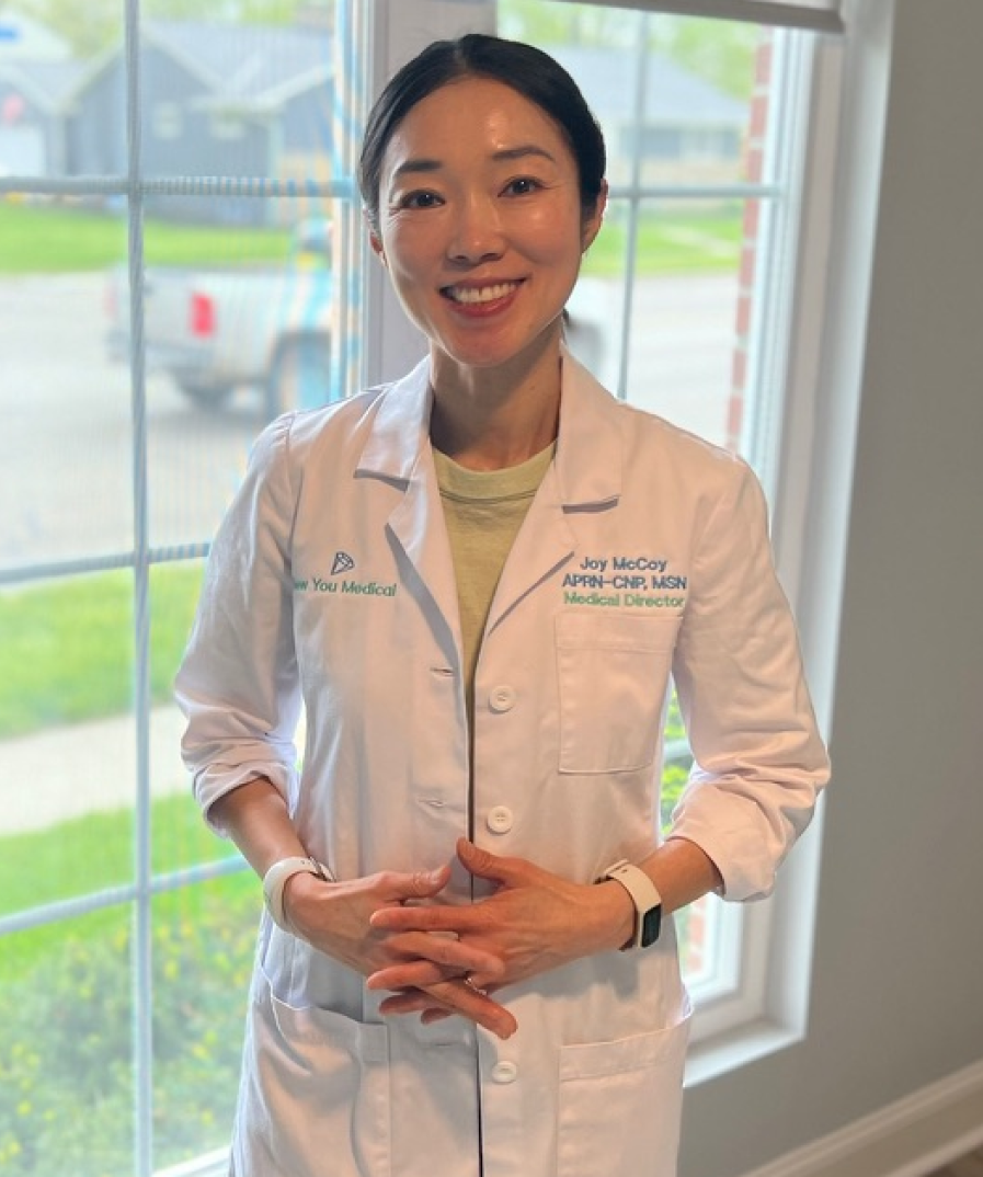 Joy McCoy, APRN-CNP, MSN, Medical Director, smiling in white lab coat by office window